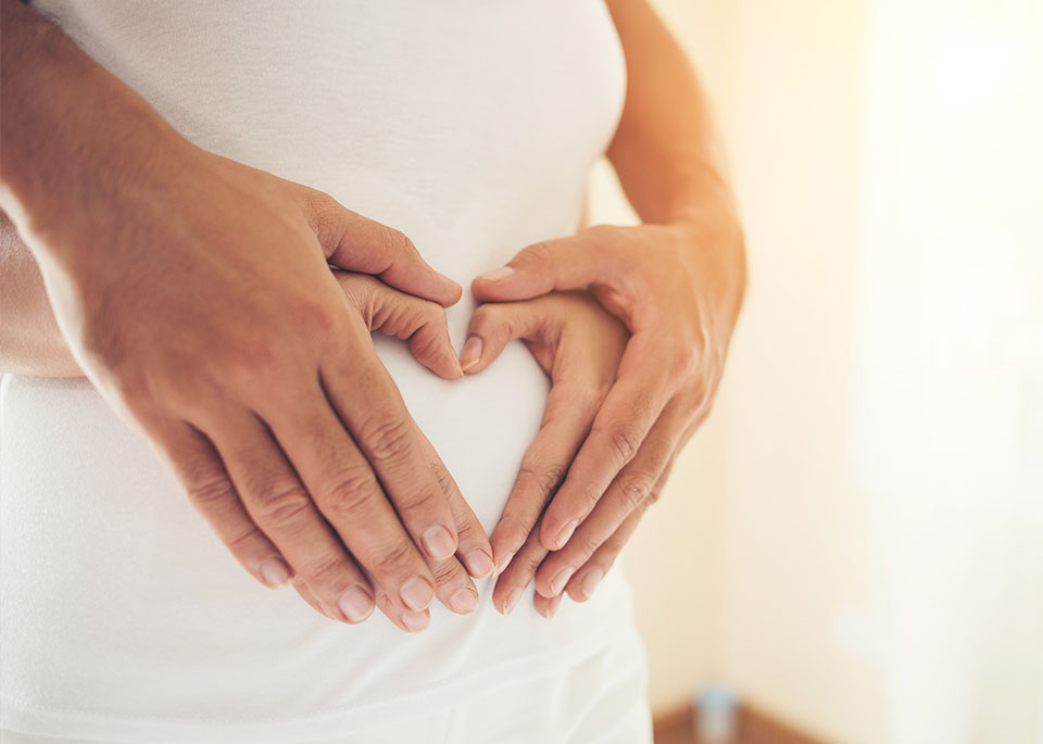 Hände auf dem Bauch einer schwangeren Frau. Hände ergeben ein Herz.